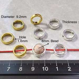 May include: A close-up of silver and gold jump rings with a hole diameter of 1.6 mm. The jump rings are arranged on a white surface with a red cord and a ruler. The jump rings are 9.2 mm in diameter and 3.2 mm thick.