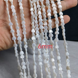 May include: A strand of white heart-shaped beads made from mother of pearl. The beads are approximately 6mm in size.