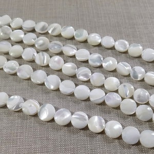 Puede incluir: Una hebra de cuentas de madreperla blanca. Las cuentas son redondas y planas, con un acabado ligeramente iridiscente.