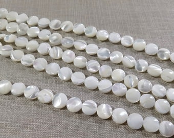 Peut inclure: Un brin de perles en nacre blanche. Les perles sont rondes et plates, avec une finition légèrement irisée.