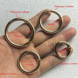 Puede incluir: Cuatro anillas de resorte de metal dorado de varios tamaños. Los anillos tienen diámetros indicados de 38mm, 31mm, 24,5mm y 19mm. El grosor se indica como 4,9mm para los dos más grandes, 4,5mm para el de 24,5mm y 3,7mm para el de 19mm.