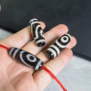May include: Three black and white agate beads with a red string threaded through them. The beads have a circular pattern of white and black.