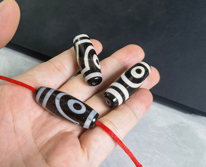 May include: Three black and white agate beads with a red string threaded through them. The beads have a circular pattern of white and black.