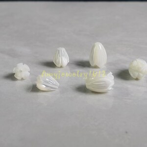 May include: A collection of six white, iridescent, carved shell beads shaped like small flower buds or tulip petals. Each bead features delicate, vertical grooves and a smooth, polished finish. The text Amyjewelry1412 is visible in yellow.