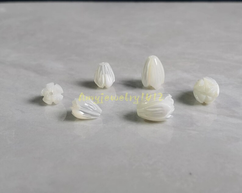May include: A collection of six white, iridescent, carved shell beads shaped like small flower buds or tulip petals. Each bead features delicate, vertical grooves and a smooth, polished finish. The text Amyjewelry1412 is visible in yellow.