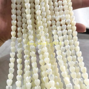 May include: Multiple strands of off-white, iridescent shell beads carved into small, tulip-like flower shapes. Each bead features vertical ridges and a smooth, pearlescent finish. The text Amyjewelry1012 is visible in yellow across the centre.