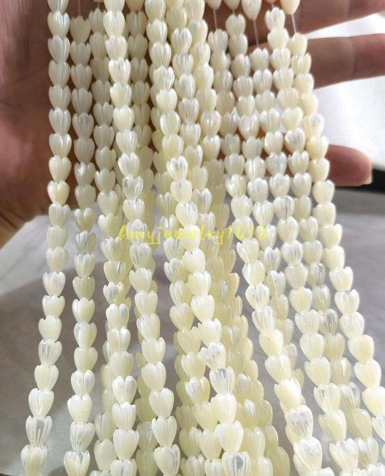 May include: Multiple strands of off-white, iridescent shell beads carved into small, tulip-like flower shapes. Each bead features vertical ridges and a smooth, pearlescent finish. The text Amyjewelry1012 is visible in yellow across the center.