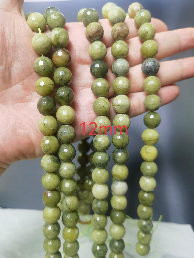 May include: A strand of green gemstone beads, each bead is faceted and measures 12mm in diameter. The beads have a mottled green color with darker green veins running through them.