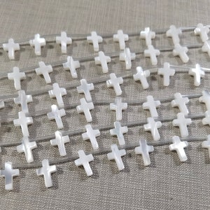Può includere: Una collana di perline a forma di croce in madreperla bianca. Le perline sono infilate su un filo elastico trasparente.