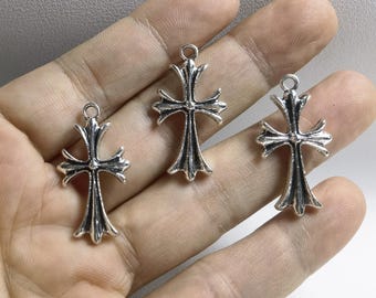 May include: Three silver cross charms with a detailed design. The crosses are hanging from a loop at the top and have a slightly textured surface.