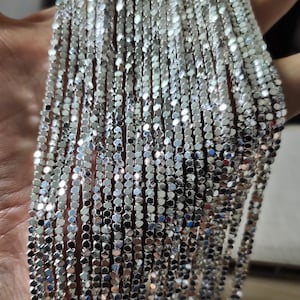 Puede incluir: Primer plano de una cadena de plata hecha de pequeños eslabones cuadrados. La cadena es brillante y reflectante, y los eslabones están estrechamente entrelazados.