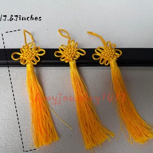 May include: Three bright yellow decorative tassels with intricate woven knots at the top and hanging loops. Each tassel measures 7.87 inches in length as indicated by the text. The tassels are arranged in a row against a black horizontal bar.