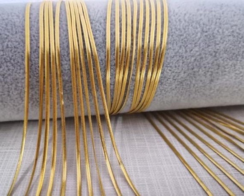 May include: A close-up of a bundle of gold-colored chain links. The chain links are thin and have a shiny finish.