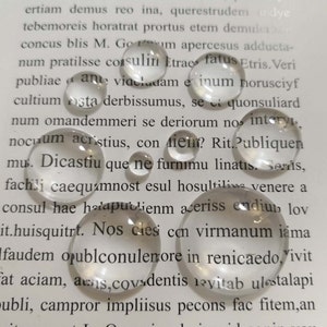 May include: A close-up of a group of clear glass beads, scattered on a page of a book. The beads are round and smooth, with a slight shimmer.