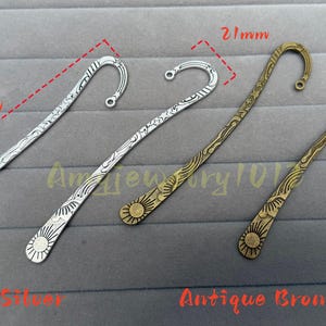 Può includere: Quattro segnalibri in metallo con un gancio curvo sulla parte superiore, caratterizzati da motivi incisi di soli e onde. Due sono in argento antico e due in bronzo antico. I segnalibri misurano 122 mm di lunghezza e 21 mm di larghezza.