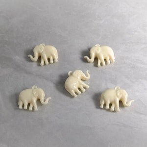 May include: Five white plastic elephant charms with a hole at the top for hanging.
