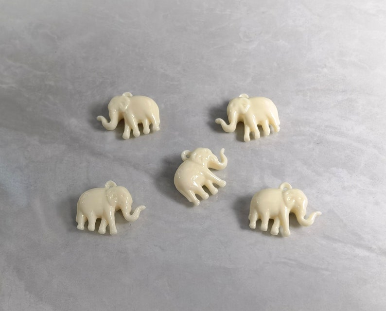 May include: Five white plastic elephant charms with a hole at the top for hanging.