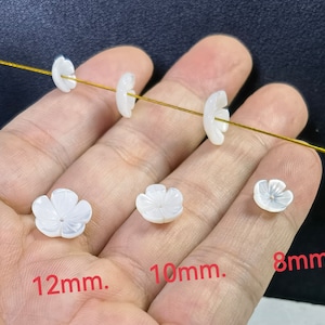 May include: Four white mother of pearl flower beads in different sizes: 8mm, 10mm, and 12mm. The beads are strung on a gold wire.