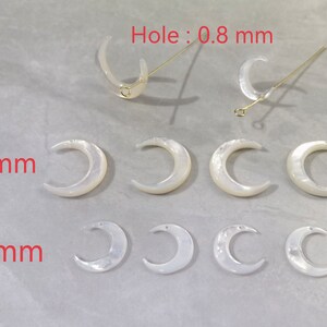 May include: White crescent moon-shaped jewelry components. The image shows several moon-shaped pieces in two sizes, 20mm and 14mm, with a hole size of 0.8 mm. Two pieces have gold-colored pins attached. The components have a pearlescent finish.