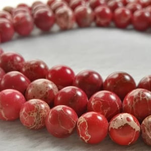 May include: A strand of red and white marbled gemstone beads. The beads are round and have a smooth, polished finish.