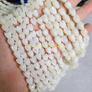 May include: Multiple strands of white mother-of-pearl beads carved into the shape of small tulip flower buds. Each bead features a smooth, iridescent surface with vertical ridges that mimic the appearance of petals on a closed flower bud.