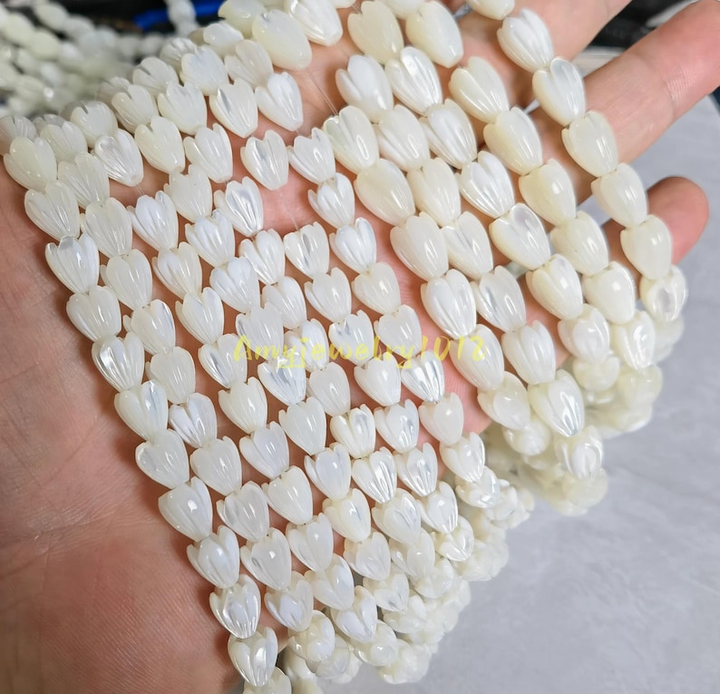 May include: Multiple strands of white mother-of-pearl beads carved into the shape of small tulip flower buds. Each bead features a smooth, iridescent surface with vertical ridges that mimic the appearance of petals on a closed flower bud.