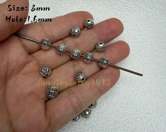 Può includere: Perline rotonde in metallo color argento con un intricato motivo a reticolo inciso. Le perline misurano 8 mm di diametro con un foro da 1,6 mm. Diverse perline sono infilate su una sottile asta di metallo, mentre altre sono sciolte.