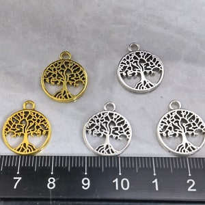 Puede incluir: Cinco dijes de plata y oro en forma de árbol de la vida. Los dijes son redondos y presentan un diseño de árbol detallado. Los dijes miden aproximadamente 2,5 cm de diámetro.