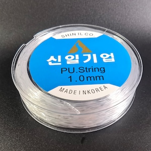May include: A spool of clear 1.0mm PU string, made in Korea. The label reads "Shin Il Co.  PU.String 1.0mm Made in Korea" in Korean and English.