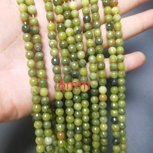 May include: A strand of green jade beads, each bead is approximately 6mm in diameter. The beads have a mottled green color with some darker green and brown streaks.