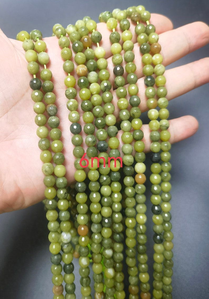 May include: A strand of green jade beads, each bead is approximately 6mm in diameter. The beads have a mottled green color with some darker green and brown streaks.