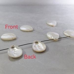 May include: A string of white mother of pearl shell beads with a black thread running through them. The beads are in the shape of a teardrop. The beads are arranged in a line with the front and back of the beads visible. The text "Front" and "Back" are written on the image.