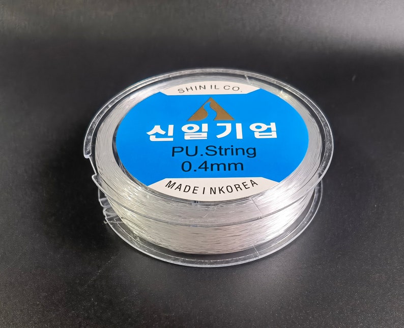 May include: A spool of clear, white, 0.4mm PU string, labeled "Shin Il Co.  신일기업 PU.String 0.4mm Made in Korea"
