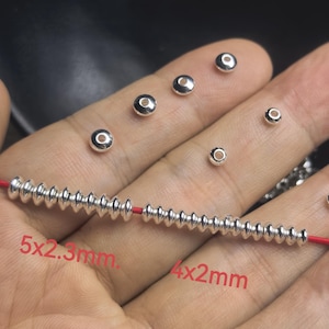 May include: Close-up of various silver beads, including a strand of small, ridged beads on a red string. The image shows several loose beads of different sizes, with text indicating sizes of 5x2.3mm and 4x2mm.