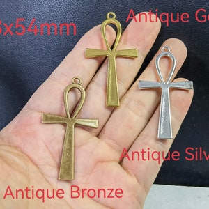 Può includere: Tre ciondoli a croce ankh che misurano 28x54mm, con finiture in bronzo antico, oro antico e argento antico. Ogni ciondolo include un piccolo occhiello circolare sulla parte superiore per il fissaggio a una catena o a un cordino.