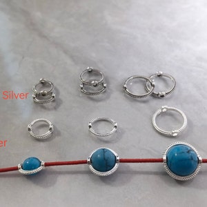 Könnte beinhalten: Ein Satz silberner und antiker silberner Sprungringe und zwei türkisfarbene Perlen mit silbernen Akzenten. Die Perlen sind auf einer roten Schnur aufgefädelt.