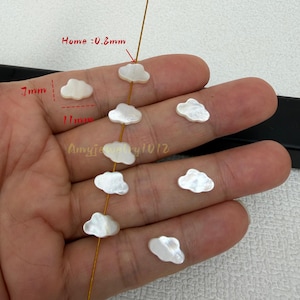 May include: White cloud-shaped beads with an iridescent finish. The beads measure 7mm in height, 11mm in width, and have a hole size of 0.8mm. Several beads are strung on a thin gold wire, while others are loose, showcasing their smooth surface.