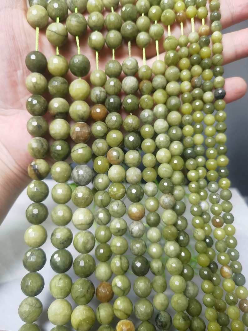 May include: A strand of green jade beads with a faceted finish. The beads are round and have a light green color with darker green veins running through them.