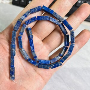 May include: A strand of blue lapis lazuli gemstone beads, each bead is a rectangular prism shape.