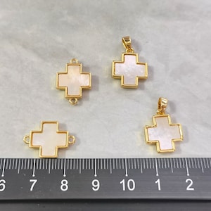 May include: Four gold-toned cross charms with white mother-of-pearl inlays. The charms are different sizes and have a loop on the top for attaching to jewelry.
