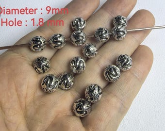Può includere: Una collezione di perline metalliche sferiche color argento con un motivo geometrico e a onde in rilievo. Le perline hanno un diametro di 9 mm e un foro di 1,8 mm. Alcune perline sono infilate su un sottile filo metallico.