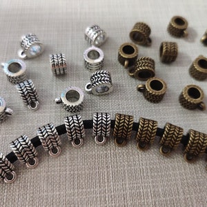 Puede incluir: Una colección de tapas de cuentas de metal plateado y bronce con un patrón de chevron decorativo. Las tapas de cuentas tienen un pequeño bucle en la parte superior para sujetarlas a las joyas.