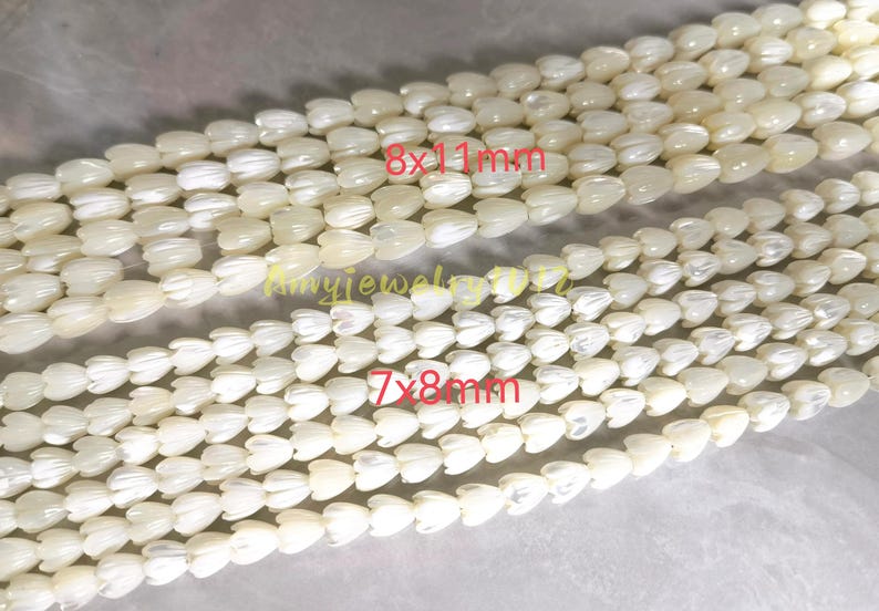 May include: Two strands of off-white, iridescent shell beads carved into tulip shapes. The top strand features beads labeled 8x11mm, while the bottom strand features smaller beads labeled 7x8mm. The text Amyjewelryvn is visible in the center.