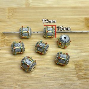 May include: Silver-toned barrel beads with gold accents, red and turquoise details, and a geometric design. Each bead is approximately 0.55 inches (14 mm) by 0.59 inches (15 mm). These beads are ideal for jewelry making.