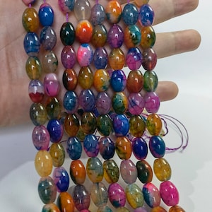 Peut inclure: Un brin de perles d'agate colorées, chaque perle est de forme ovale et présente un motif unique de couleurs tourbillonnantes, y compris des nuances de bleu, de vert, de rose, d'orange et de jaune.
