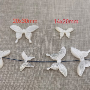 May include: Five white mother of pearl butterfly charms, two are 20x30mm and three are 14x20mm. The charms are strung on a black thread.