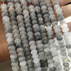 Könnte beinhalten: Eine Strähne aus grauen und weißen, mattierten Glasperlen. Die Perlen sind rund und haben eine glatte, polierte Oberfläche.