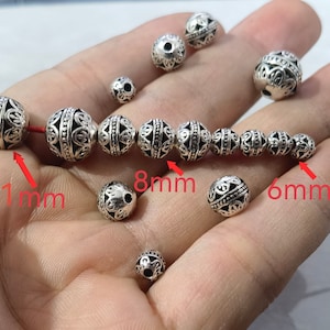 May include: A collection of round, silver-toned metal beads featuring intricate filigree patterns and black recessed detailing. The beads are shown in various sizes, with red text labels indicating specific diameters of 11mm, 8mm, and 6mm.