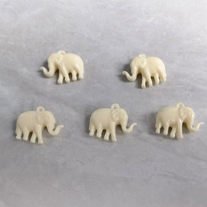 May include: Five white plastic elephant charms with a loop for hanging. The elephants are all facing the same direction and have a raised trunk.