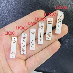 Puede incluir: Siete piezas rectangulares de concha blanca con diferentes diseños tallados. Las piezas están etiquetadas con los números LK001 a LK007.